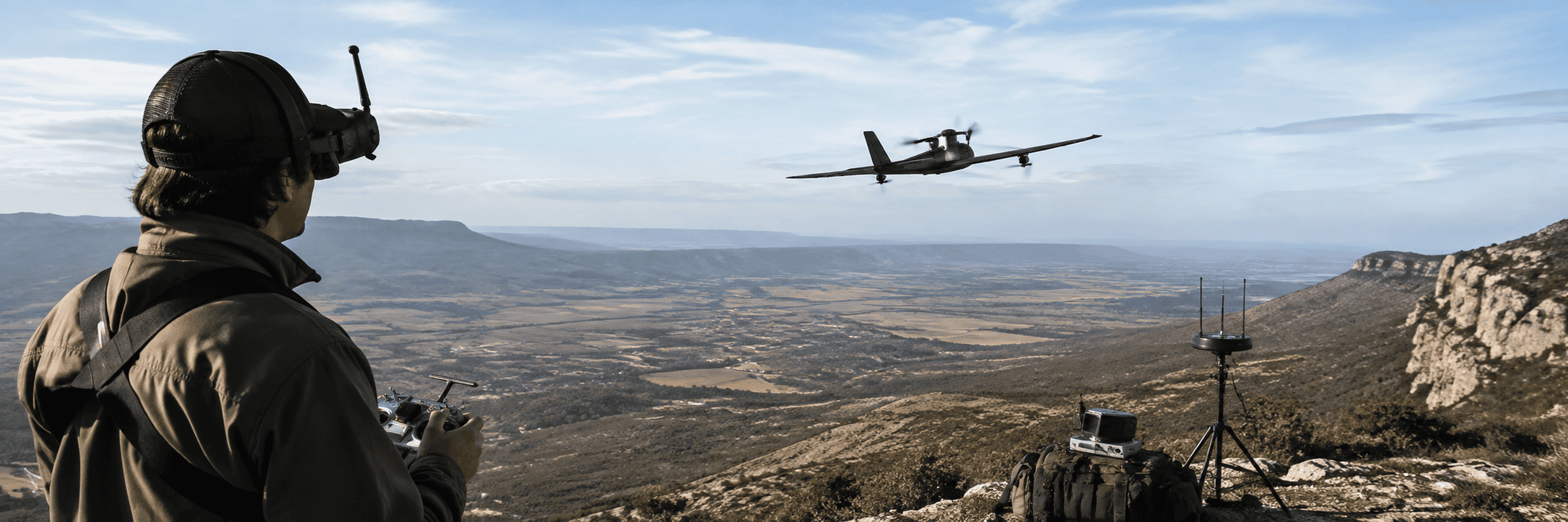 Long-range FPV aircraft flying over open terrain with a radio controller at the launch point.