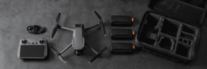 Compact camera drone, controller and individually protected batteries arranged beside an open carry-on case.