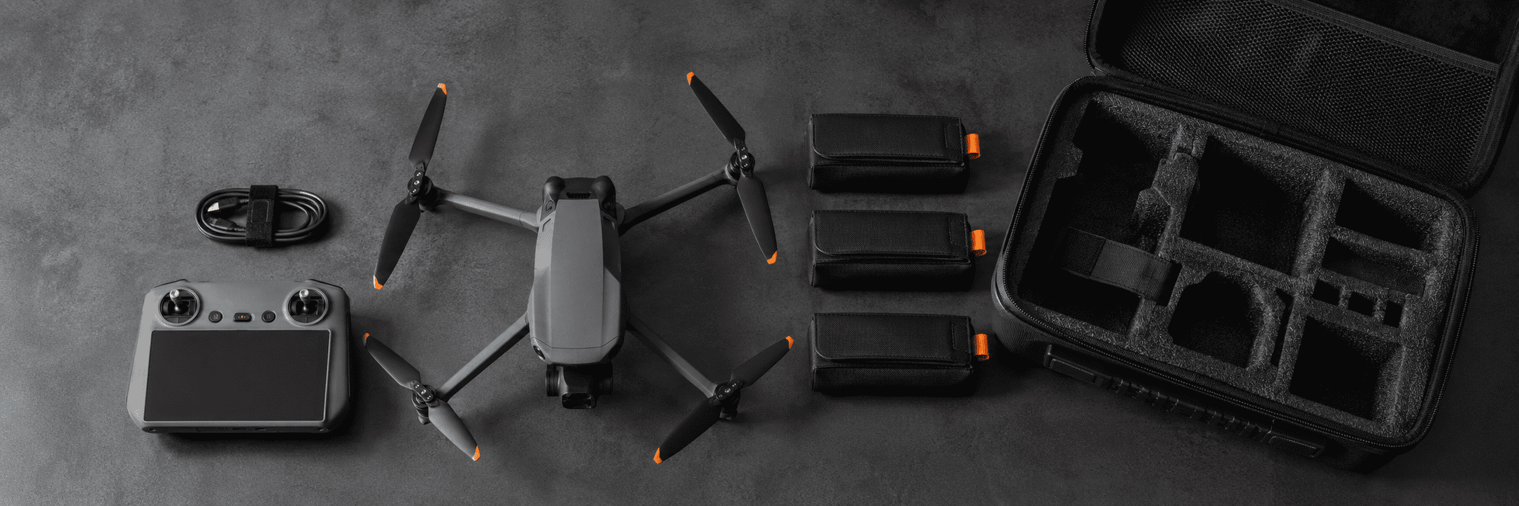 Compact camera drone, controller and individually protected batteries arranged beside an open carry-on case.