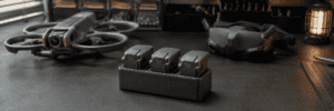 Three intelligent-flight batteries in a charging hub beside a cinewhoop drone and FPV goggles.