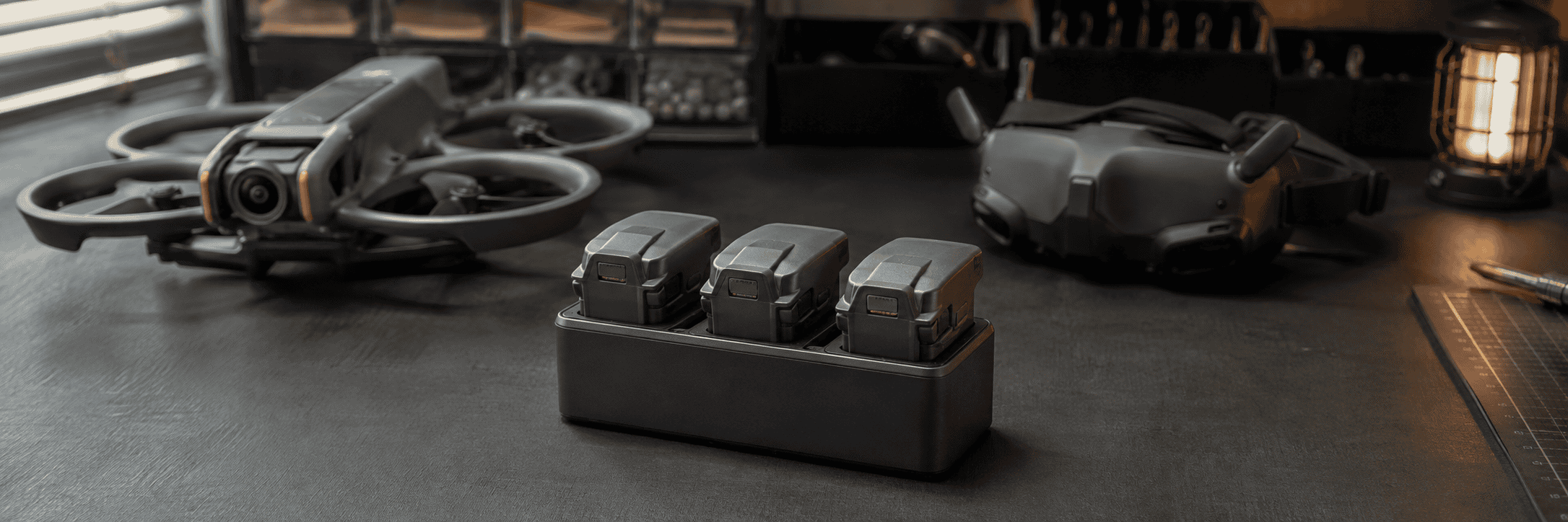 Three intelligent-flight batteries in a charging hub beside a cinewhoop drone and FPV goggles.