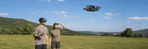 A DJI Avata 2 pilot wearing goggles flies beside a visual observer watching the aircraft in an open field.