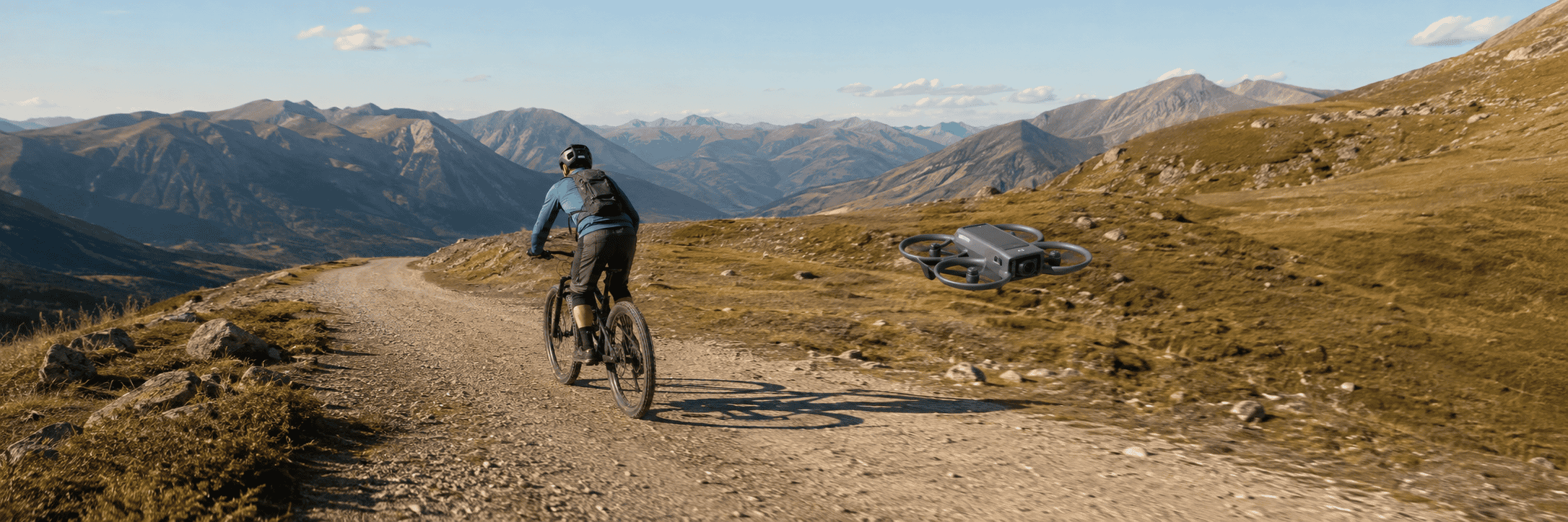 Generic enclosed-prop follow-me drone tracking a mountain biker on an open gravel trail.