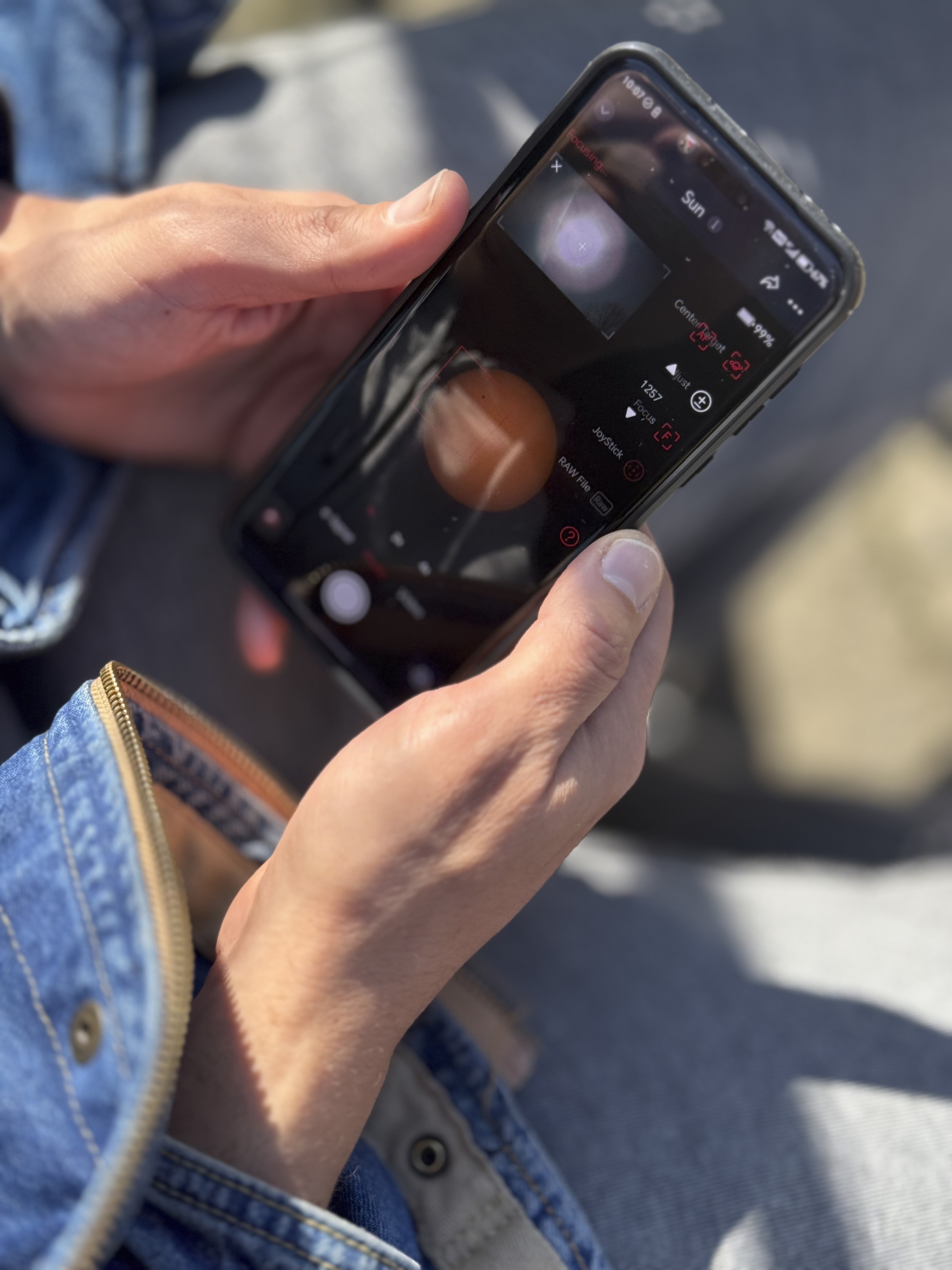 Hands holding a smartphone with camera controls visible on its screen outdoors