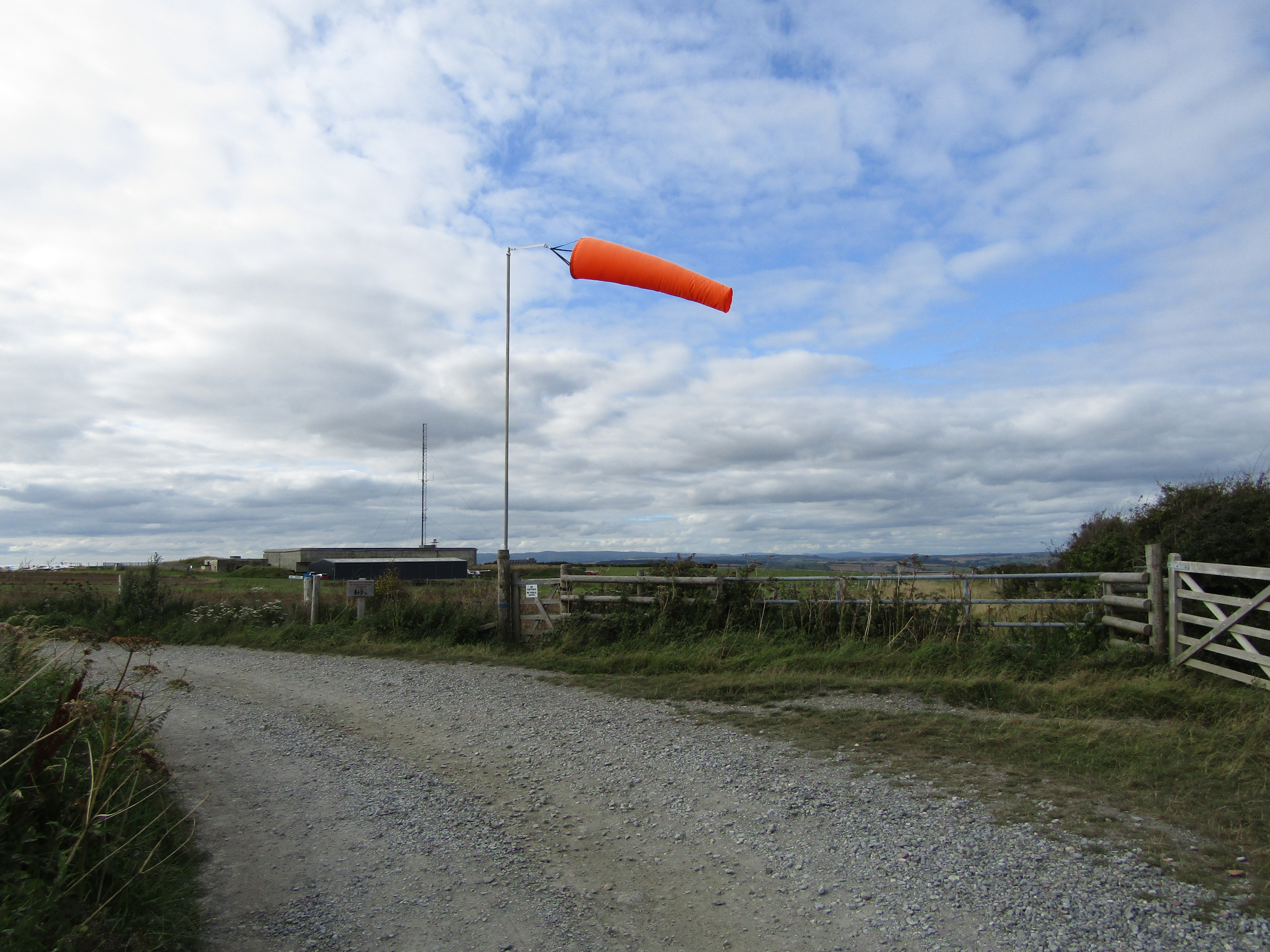 An orange windsock extends to the right above an open airfield beneath broken cloud.